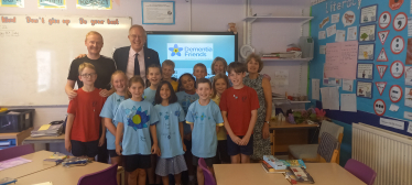 Photo shows John with Headteacher, Michael Wade, and pupils and staff at the school.